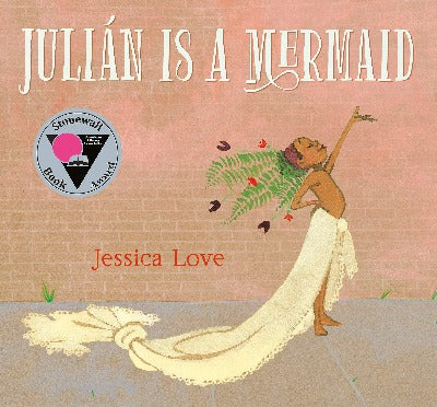 Julian stands proudly in front of a brick wall with ferns and flowers in his hair and a long curtain draped around his waist. He looks like a mermaid. 