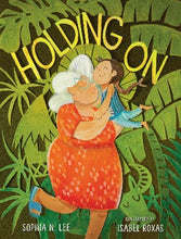 a grandmother with white hair, glasses and wearing an orange dress is holding up a young girl. They are furrounded by lush foliage.